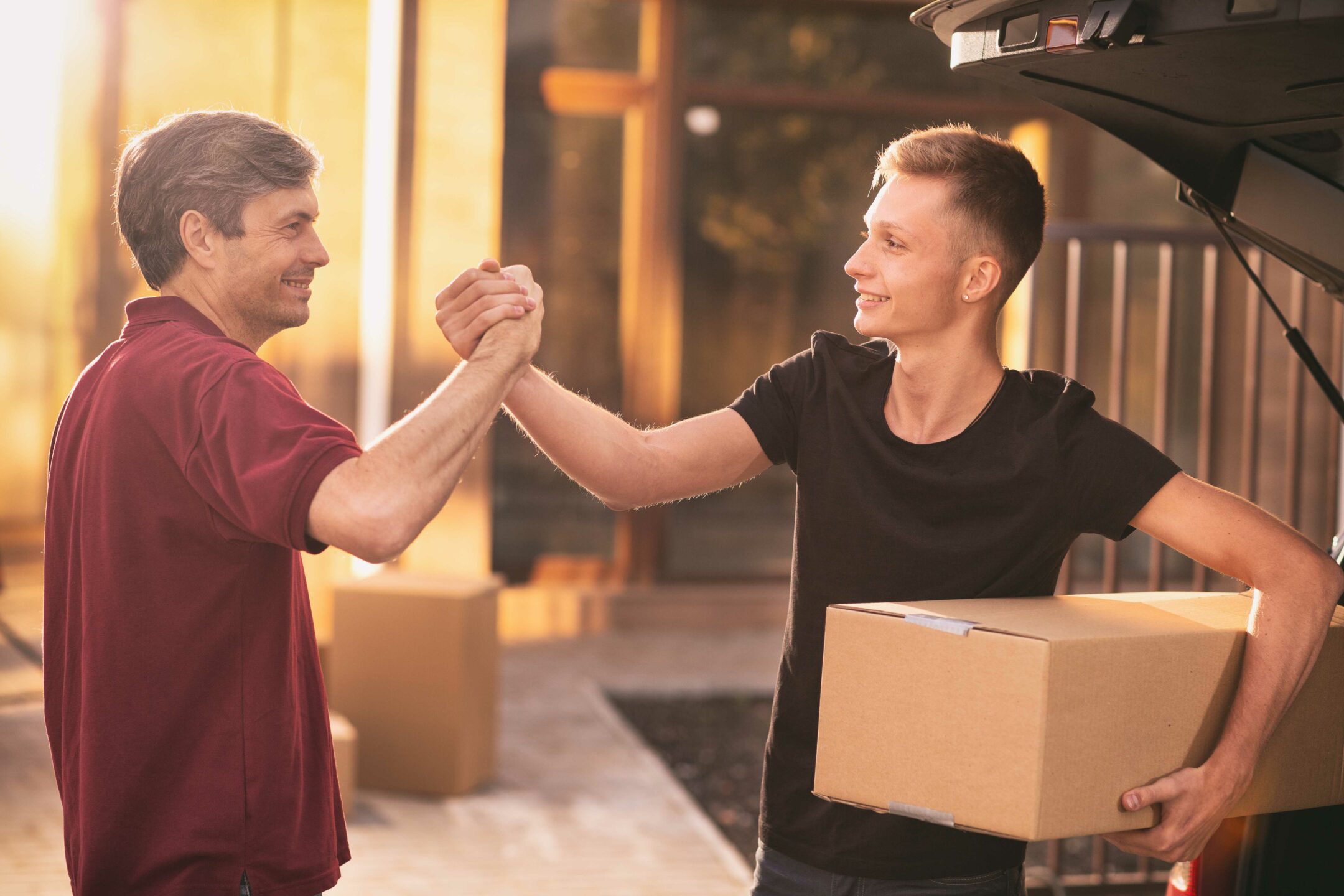 Student Loans. Teenage boy shaking hands with his father while moving into their new home together, carrying cardboard boxes. Single parent concept