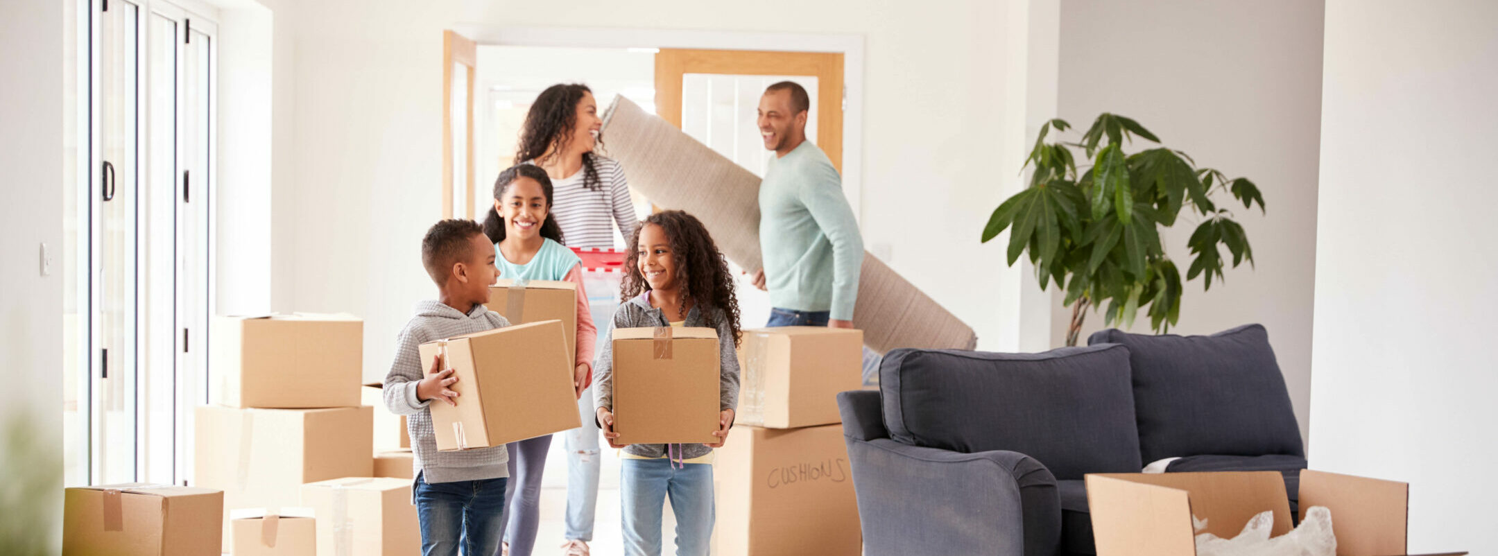Smiling Family Carrying Boxes Into New Home On Moving Day