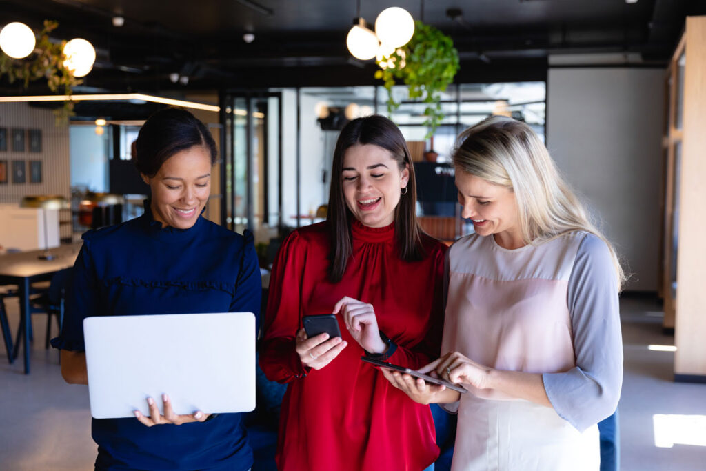 Three professional women looking at their phones and laptops